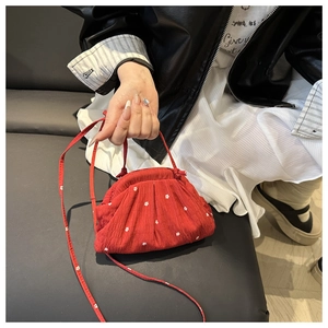 Détail du sac à bandoulière rouge à fleurs avec tissu texturé sur la main du modèle
