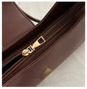 Detail view of smooth golden metal zipper and brown leather texture on handbag