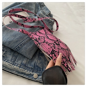 Detail of pink and black snakeskin crossbody bag with long fringes on denim jacket