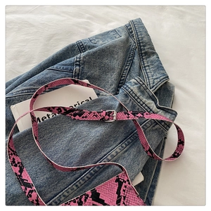 Detailed shot of pink snakeskin pattern strap with silver metal buckle on denim fabric