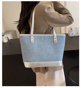Detail of denim tote bag with silver leather trim and metal logo on a side view model