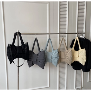 Row of puffer bow bags in black, grey, blue, khaki, and cream hanging on a wall