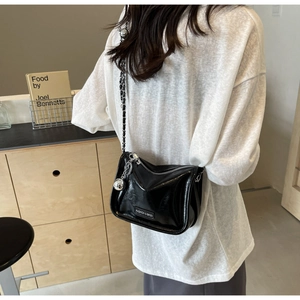 Détail du sac bandoulière noir brillant avec chaîne argentée et breloque en métal