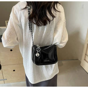 Détail d'un sac à bandoulière noir brillant avec chaîne argentée et pendentif boule