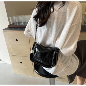 Détail d'un sac bandoulière en cuir verni noir avec chaîne et breloque boule argentée