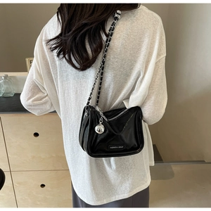 Détail d'un sac noir brillant à chaîne avec breloque sphérique porté au dos