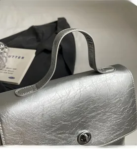 Détail de la poignée du sac argenté avec texture craquelée et fermoir rotatif en métal