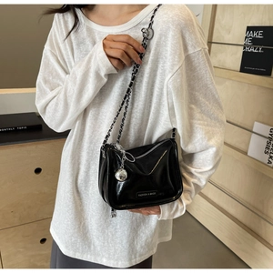 Détail du sac bandoulière noir brillant avec chaîne argentée et charm boule en métal