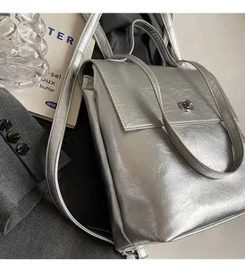 Gros plan du sac à dos argenté avec texture froissée et fermoir pivotant sur un costume gris