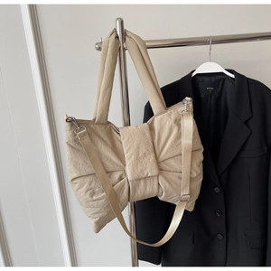 Detail of beige puffer tote bag with ribbon design and adjustable woven shoulder strap