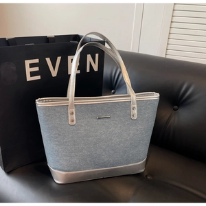 Detail of blue denim tote bag featuring silver leather trim and metal logo ornament