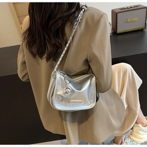 Détail d'un sac à bandoulière argenté métallisé avec chaîne et breloque sphère sur modèle