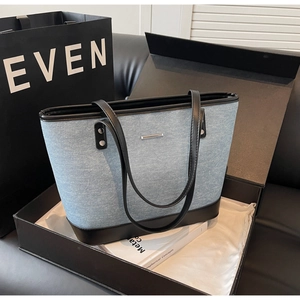 Close-up of a blue denim tote bag with black leather trim inside a premium gift box