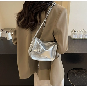 Détail d'un sac en cuir argenté avec bandoulière chaîne porté par un mannequin
