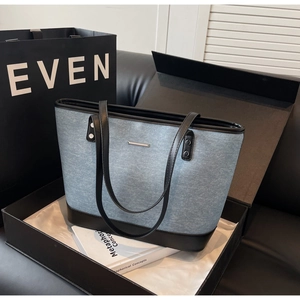 Detail of blue denim tote bag with black leather trim and silver metal bar in gift box