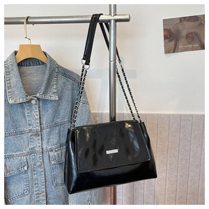 Detail view of black patent leather quilted shoulder bag with silver chain and metal buckle