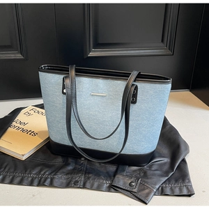 Detail of blue denim tote bag featuring black leather trim and silver metal hardware