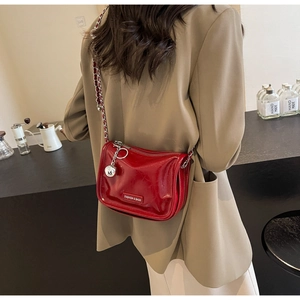 Détail d'un sac à bandoulière en cuir verni rouge avec chaîne argentée porté par un mannequin