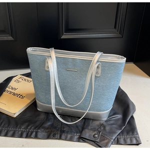 Detail of blue denim tote bag with silver leather trim on dark background
