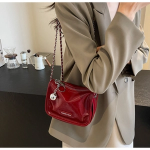 Détail du sac à bandoulière en cuir verni rouge avec chaîne argentée et pendentif boule