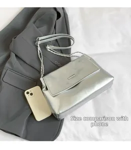Close-up of silver quilted shoulder bag with chain strap comparing size to a smartphone