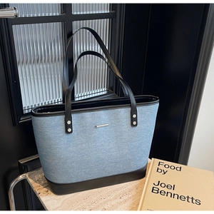 Detail of light blue denim tote bag with black leather base and metallic silver bar