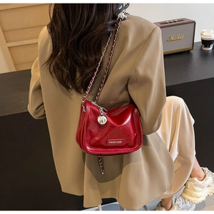 Détail du sac croissant en cuir verni rouge avec chaîne en métal et pendentif argent