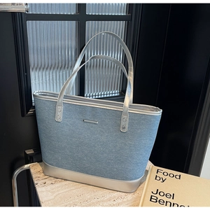 Detailed shot of large denim tote bag with silver leather trim on marble surface