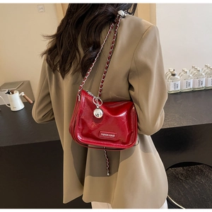 Détail du sac bandoulière en cuir verni rouge avec chaîne argentée et breloque boule