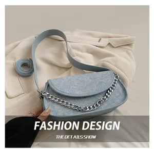 Detail of light blue denim saddle bag with chunky silver chain on soft bedding
