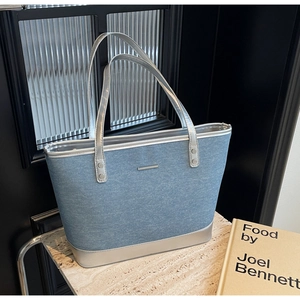 Detail view of denim tote bag with silver leather trim and minimalist metal accent