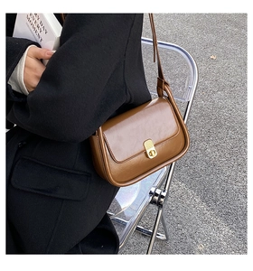 Detail of vintage brown leather crossbody bag with elegant gold lock on model shoulder