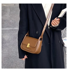 Close-up of brown vintage crossbody bag featuring a gold square buckle and rivet strap