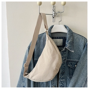 Detail of a beige crescent crossbody bag against a denim jacket backdrop