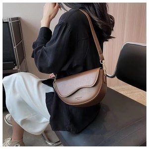 Close-up of a brown saddle bag with wavy flap design and gold buckle on a model