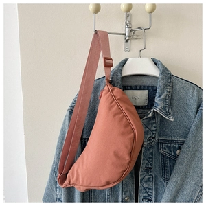 Detail of dusty rose crescent crossbody bag hanging on a denim jacket background