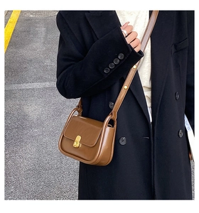 Detail of a vintage brown leather crossbody bag styled with a long black winter coat