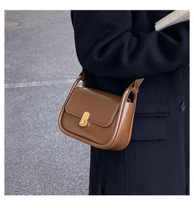 Detail of caramel leather shoulder bag with a rectangular gold twist lock on navy coat