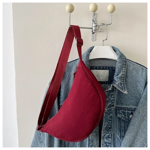 Side view of a burgundy crescent crossbody bag hanging on a denim jacket.