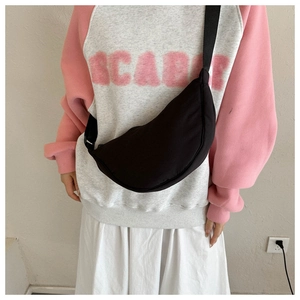 Minimalist black crescent crossbody bag with wide shoulder strap worn across the chest