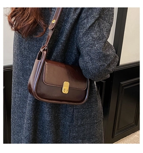 Detail of vintage brown patent leather crossbody bag with a gold retro clasp on a coat