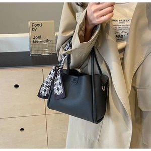 Dettaglio di una borsa a secchiello in pelle martellata nera con un elegante foulard di seta