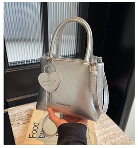 Detail of silver metallic bucket bag with heart pendant and brand lettering on leather
