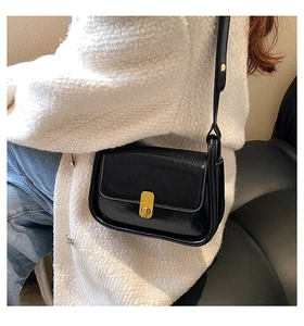 Detail of vintage black glossy leather shoulder bag with a gold clasp on an ivory jacket