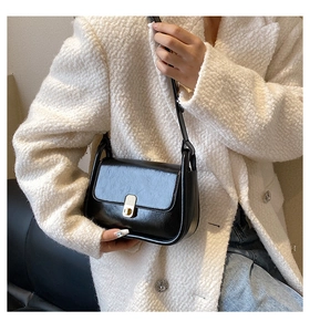 Close-up of black polished leather shoulder bag with gold metal buckle on white coat
