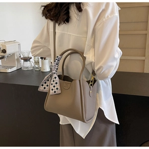 Dettaglio borsa a secchiello in pelle martellata con foulard decorativo sulla spalla