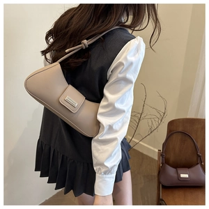Side view of a beige minimalist baguette bag on woman shoulder in soft natural light