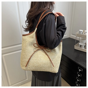 Détail du sac cabas en paille tissée main avec anses en cuir marron et nœud décoratif