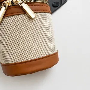 Detail of canvas cylinder bag featuring brown leather trim and golden metal dual zippers