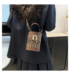 Detail of leopard print cylinder bag with brown leather trim and gold double zippers